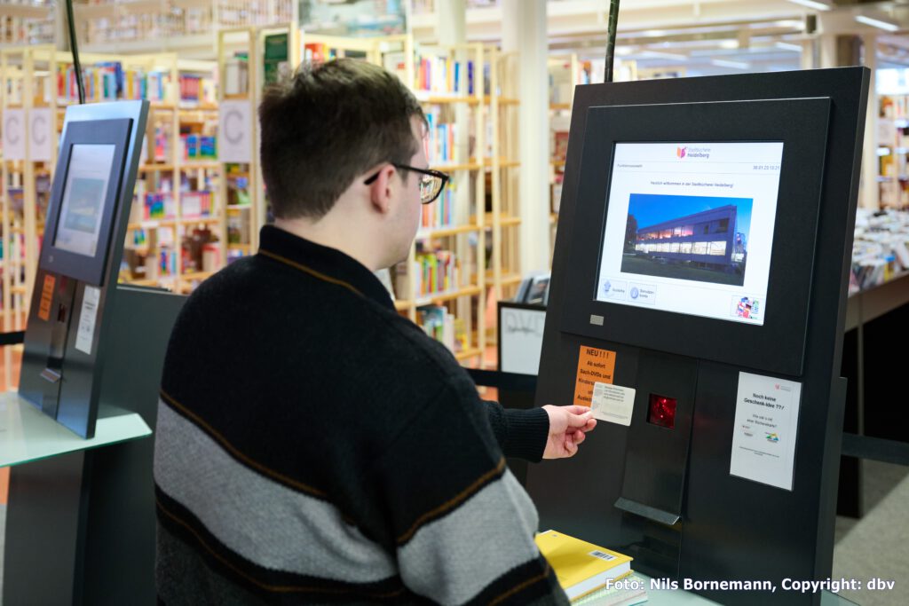 Mann leiht mit der Metropol-Card Bücher in der Bücherei an der Selbstverbuchungsanlage aus